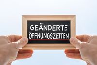 Schild mit der Aufschrift 'Geänderte Öffnungszeiten' in den Händen einer Person.