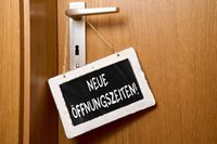 Schild mit der Aufschrift 'Neue Öffnungszeiten!' hängt an einer Türklinke.