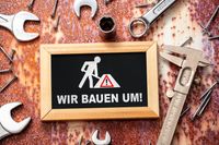 Schild mit der Aufschrift 'Wir bauen um!' umgeben von Werkzeugen und Schrauben.