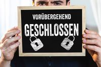 Schild mit der Aufschrift 'Vorübergehend geschlossen', gehalten von einer Person.