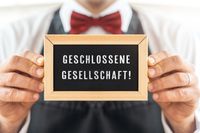 Schild mit der Aufschrift 'Geschlossene Gesellschaft!' gehalten von einem Kellner in roter Fliege.