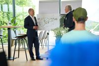 Bundeskanzler Olaf Scholz während einer Diskussion im Olympiapark München zur Fußball-Europameisterschaft 2024. Scholz steht neben einem Flipchart und spricht über die geplanten Maßnahmen. Im Vordergrund sind Zuhörer zu sehen.