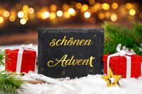 Schönen Advent auf schwarzem Schild als Adventsgruß mit goldener Schrift, umgeben von weihnachtlicher Dekoration.