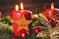 Rote Kerze mit Stern-Dekoration und der Aufschrift schönen 1 Advent, umgeben von einem festlichen Adventskranz.