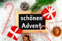 Schönen Advent auf Tafel mit Weihnachtsdekoration, Geschenken, Zuckerstangen und Tannenzweigen im Schnee.