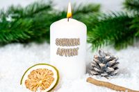 Weiße Adventskerze mit „Schönen Advent“, dekoriert mit Tannenzweigen, Tannenzapfen und Orangenscheibe.