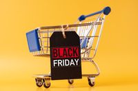 Einkaufswagen mit Black Friday Schild auf gelbem Hintergrund – Symbol für Black Friday Angebote und Sonderpreise.