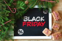 Weihnachtlich dekorierte Tafel mit der Aufschrift Black Friday, umgeben von Geschenken zu Weihnachten – ein Symbol für Black Friday Angebote.