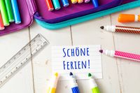 Eine Notiz mit der Aufschrift ‚Schöne Ferien!‘ umgeben von bunten Stiften, Lineal und Federmäppchen, ideal als Urlaubsgrüße und Urlaubssprüche für schöne Ferien.