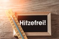 Thermometer neben einer Tafel mit der Aufschrift ‚Hitzefrei‘, passend zur Situation, wenn die Schule oder das Büro wegen Hitze geschlossen ist.