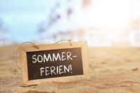 Schild am Strand mit der Aufschrift: Sommerferien, bei Sonnenuntergang, passend zu den Sommerferien 2025.