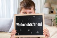 Ein Schüler hält eine Tafel mit der Aufschrift ‚Weihnachtsferien‘, passend zu den Weihnachtsferien 2025.