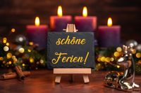 Tafel mit der Aufschrift ‚schöne Ferien!‘ vor einem festlichen Hintergrund mit Kerzen und Weihnachtsdekoration, passend zu den Weihnachtsferien 2025, im Winterurlaub..