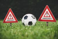 Ein Fußball liegt auf dem Rasen zwischen zwei Schildern mit der Aufschrift 'Abgesagt!' – Symbol für ein abgesagtes Fußballspiel.