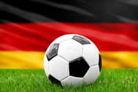 Ein Fußball auf einem Spielfeld vor der Deutschlandflagge, symbolisch für die deutsche Nationalmannschaft.