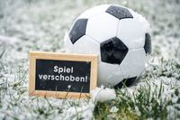 Ein Fußball im Schnee neben einem Schild mit der Aufschrift 'Spiel verschoben'.