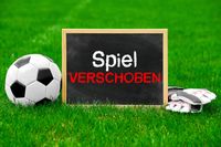 Fußball und Torwarthandschuhe neben einer Tafel mit der Aufschrift 'Spiel verschoben' auf einem Spielfeld.