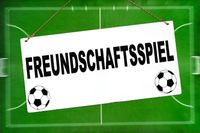 Schild mit der Aufschrift 'Freundschaftsspiel' vor einem Fußballfeld, symbolisch für ein Fußball-Freundschaftsspiel.