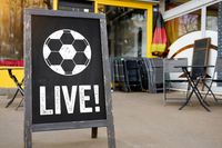 Fußball live Ankündigung auf einer Tafel vor einem Restaurant mit Deutschland-Flagge.