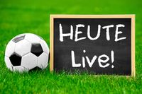 Fußball neben einer Tafel mit der Aufschrift 'Heute Live!' auf einem Spielfeld.