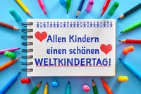 Ein Schulbuch mit der Aufschrift ‚Allen Kindern einen schönen Weltkindertag!‘, umgeben von bunten Malstiften und Markern. Das Bild drückt die Freude und Wertschätzung zum Weltkindertag aus.