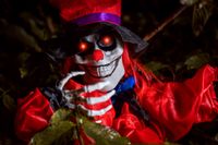 Gruseliger Clown als Geist mit Maske und rotem Halloweenkostüm mit leuchtenden roten Augen im dunklen Wald.