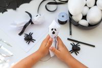 Kinderhände basteln ein kleines Geister-Kostüm-DIY Halloweenkostüm für Halloween mit Stoff und schwarzen Stiften.