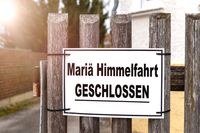 Ein Schild mit der Aufschrift „Mariä Himmelfahrt GESCHLOSSEN“ hängt an einem Holzzaun.