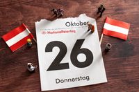 Kalenderblatt mit dem Datum „26. Oktober“ und der Aufschrift „Nationalfeiertag“ in Österreich, umgeben von kleinen österreichischen Flaggen und Menschen.