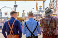 Drei Männer in traditioneller bayrischer Tracht mit Lederhosen, die über das Oktoberfest schlendern.