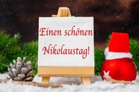 Einen schönen Nikolaustag! auf Leinwand mit Nikolausdeko im Schnee mit Mütze vom Nikolaus.