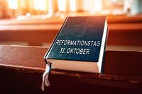 Ein Gebetbuch mit der Aufschrift 'Reformationstag 31. Oktober' liegt auf einer Kirchenbank – Darstellung kirchlicher Bräuche.