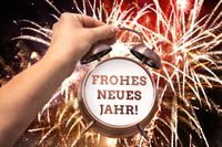 Neues Jahr Wünsche: Hand hält Wecker mit 'Frohes neues Jahr!' vor Feuerwerk.