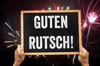 Guten Rutsch. Tafel mit Guten Rutsch Aufschrift, Feuerwerk zum Jahreswechsel im Hintergrund.