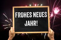 Frohes neues Jahr, steht auf einer Tafel, die eine Person vor Feuerwerk an Neujahr hält.