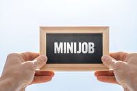 Hände halten ein Schild mit der Aufschrift „Minijob“, das auf ein Stellenangebot hinweist