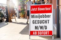 Ein Aufsteller vor einem Geschäft mit der Aufschrift „Minijobber gesucht M/W/D – ab sofort“ und „Jetzt Bewerben!“ signalisiert eine Stellenausschreibung.