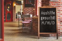 Aushilfe gesucht! M/W/D, steht auf einem Kundenstopper vor einem Restaurant und signalisiert eine Stellenausschreibung für eine Aushilfskraft.