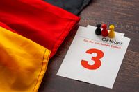 Kalenderblatt mit dem 3. Oktober, Tag der Deutschen Einheit, neben einer deutschen Flagge und Spielfiguren in Schwarz, Rot und G