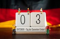 Kalender mit dem Datum 3. Oktober, Tag der Deutschen Einheit, im Vordergrund mit Miniaturfiguren und deutscher Flagge im Hinterg