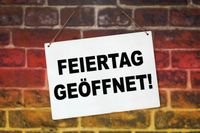 Schild mit der Aufschrift 'Feiertag geöffnet' vor einer Backsteinwand, symbolisch für geöffnete Geschäfte am Feiertag.