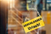 Gelbes Schild mit der Aufschrift: geschlossen wegen Urlaub, hängt an einer Glastür, beleuchtet von warmem Sonnenlicht.