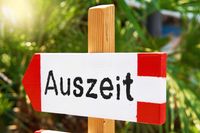 Auszeit steht auf einem Schild, vor einer grünen, sonnigen Urlaubs-Kulisse.