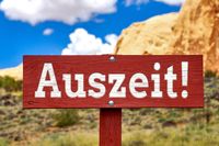 Auszeit als Wort für den Urlaub auf roten Schild vor einer schönen Landschaft mit Felsen und blauem Himmel.