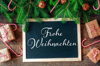 Tafel mit Frohe Weihnachten Schriftzug, umgeben von Tannenzweigen und Geschenken.