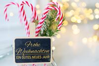 Tafel mit der Aufschrift ein frohes Weihnachtsfest und ein gutes neues Jahr umgeben von Zuckerstangen und weihnachtlichem Licht.