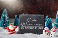 Schneemann und Weihnachtsmann vor winterlicher Schieferplatte.