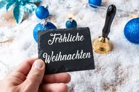 Eine Hand hält eine Schiefertafel mit der Aufschrift fröhliche Weihnachten.