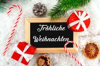 Eine Tafel mit Fröhliche Weihnachten Schriftzug, umgeben von typischen Weihnachtsgrüßen.