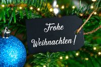 Frohe Weihnachten wünschen mit einer schwarzen Karte und blauer Weihnachtskugel am Baum.